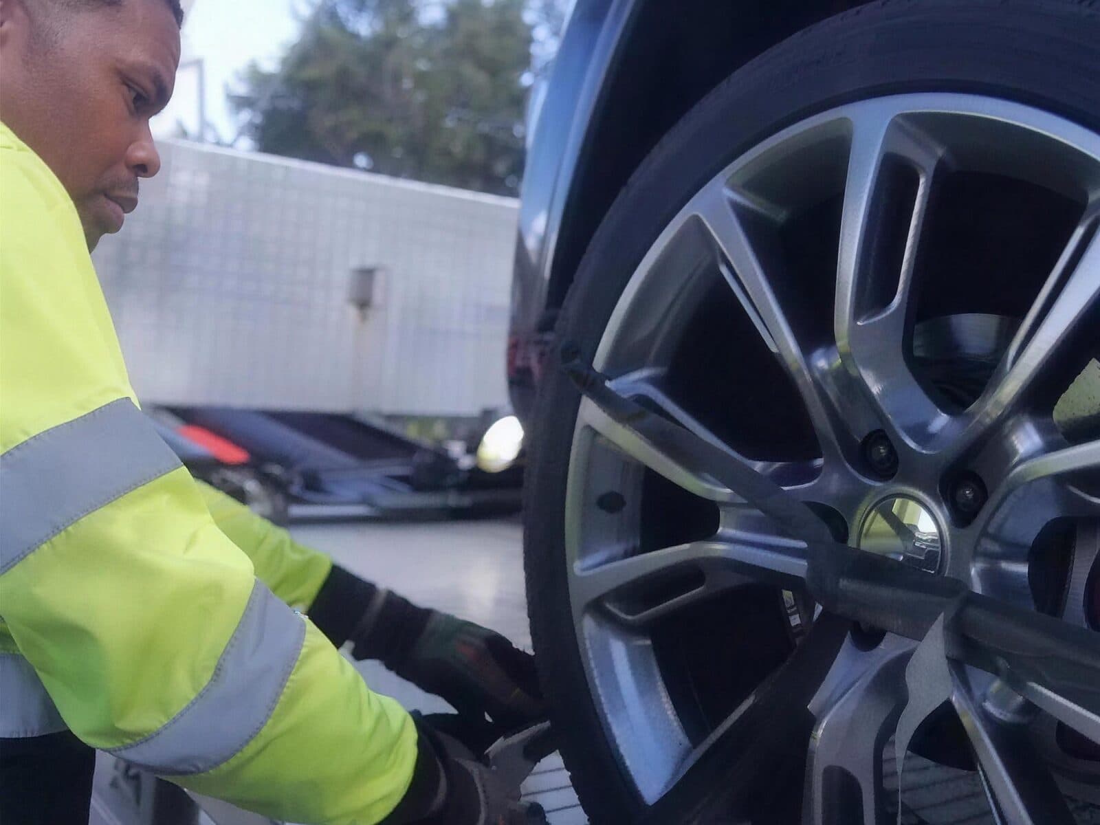 Crouched at a wheel in a hi-vis vest, working on the tire at the side of the flatbed