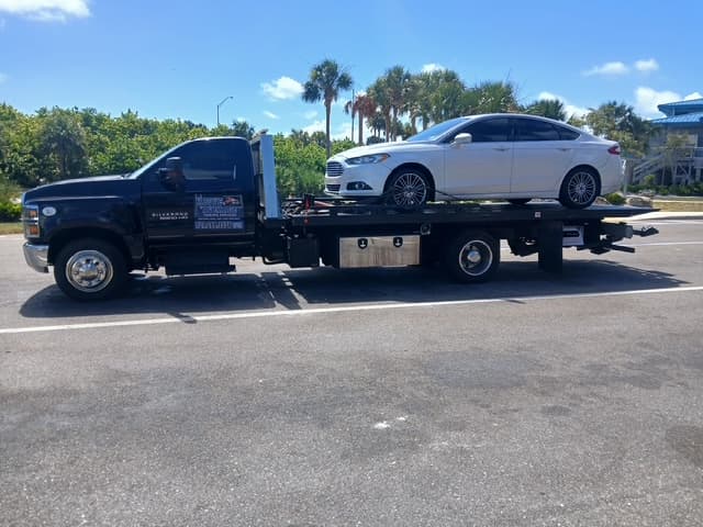 White Ford Fusion sedan riding on the flatbed with palm trees behind