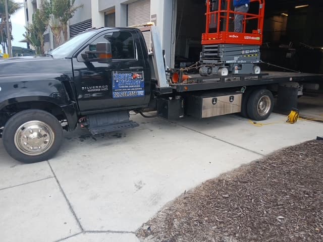 The flatbed loading a scissor lift at a job site, door decal in view
